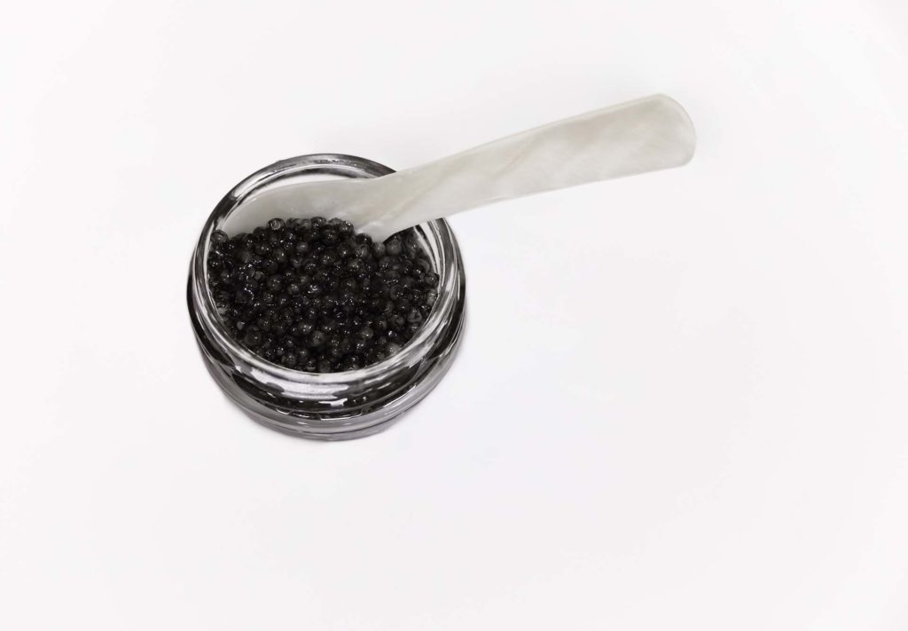 Isolated jar of sustainably farmed black sturgeon caviar with a mother-of-pearl spoon