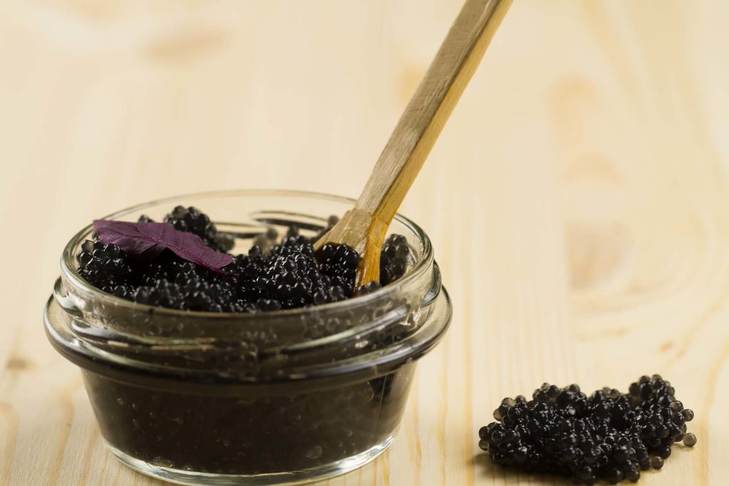 black Beluga caviar in glass jar on wooden background