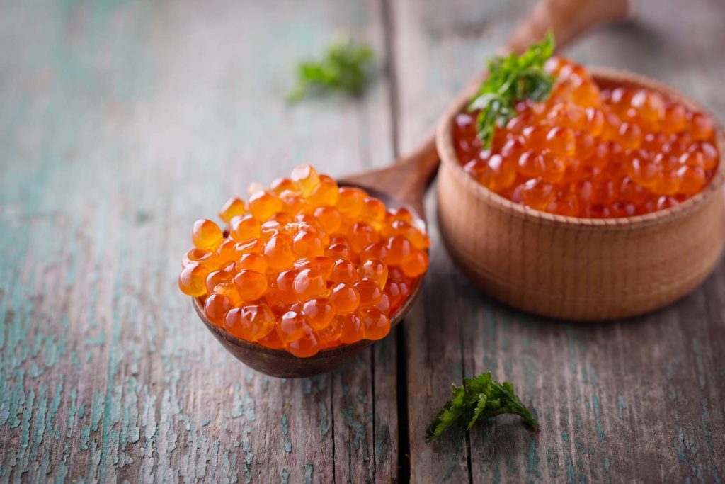 Red caviar on aged wooden background. Selective focus is in caviar in spoon.
