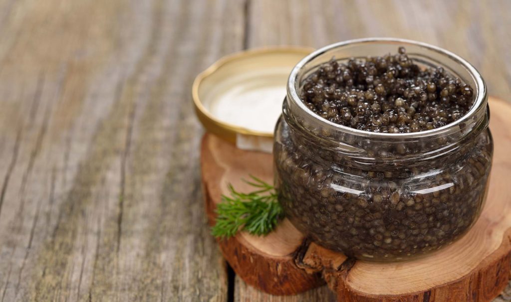 Natural black caviar in a glass jar on a wooden background