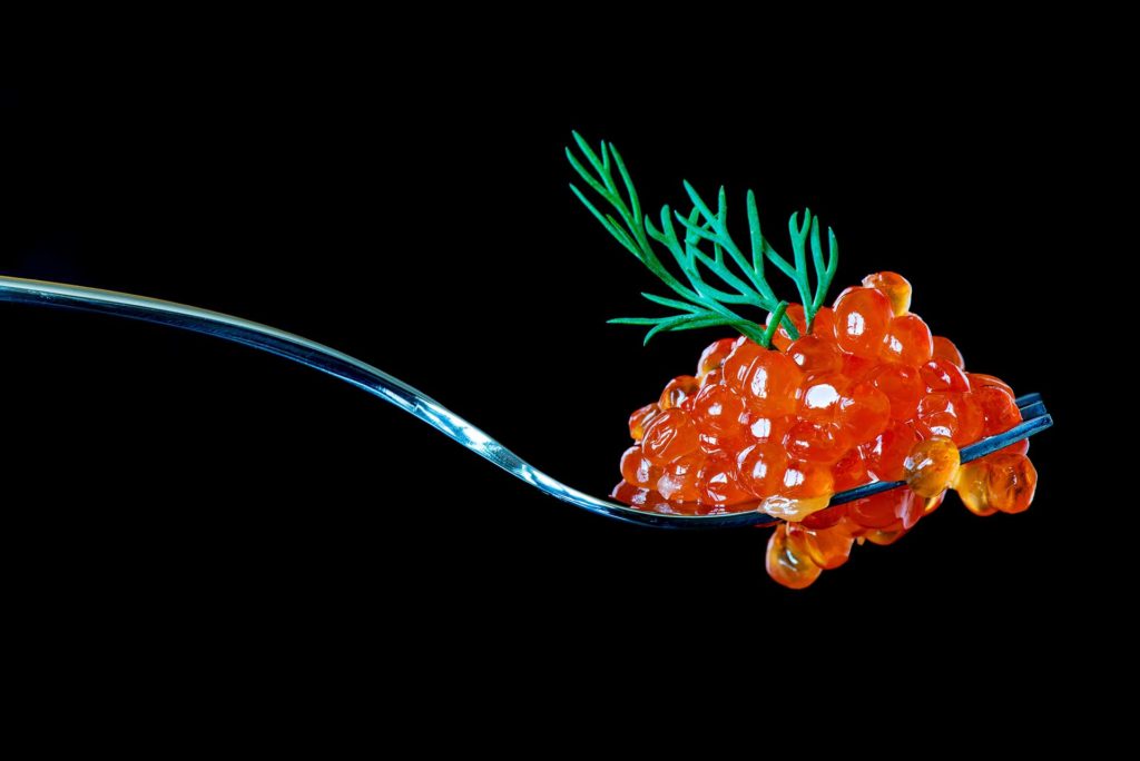 Red caviar on a metal fork isolated on black background