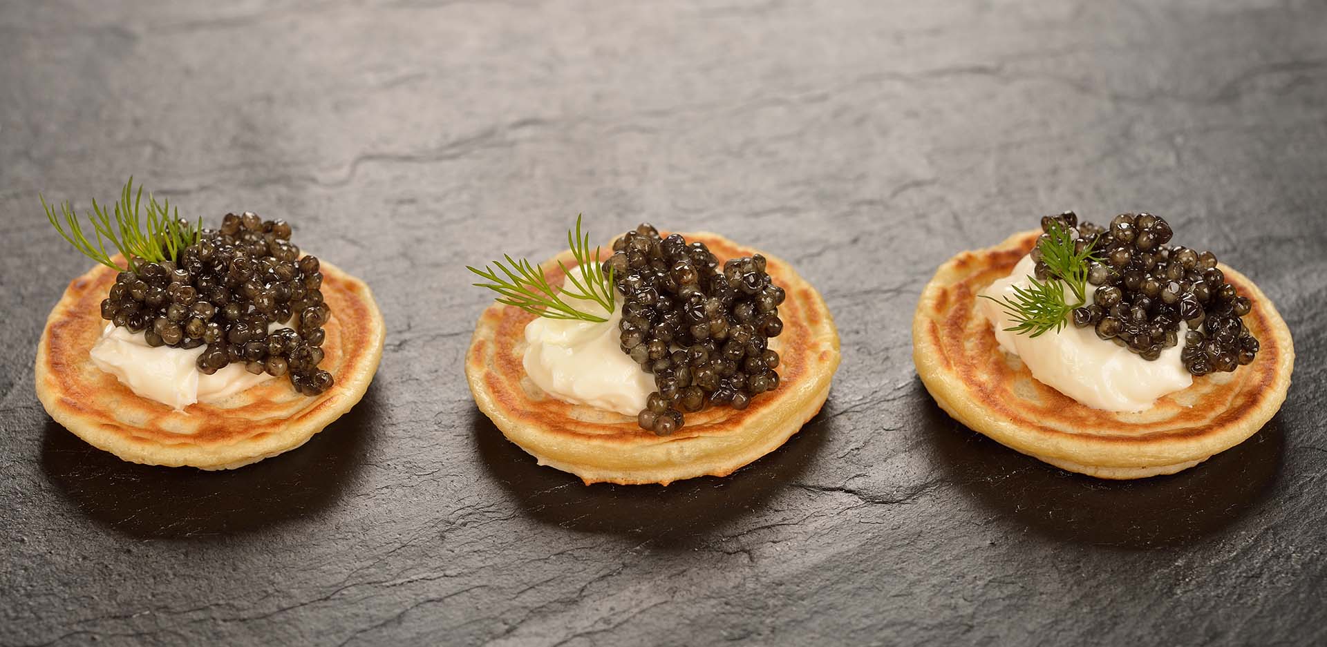 Mini pancakes with black caviar on a black background
